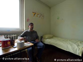 An asylum seeker sits in his barren room