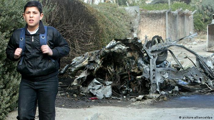  An Iraqi boy passes by the remains of a car used in a bomb attack at Yarmuk district, in Baghdad