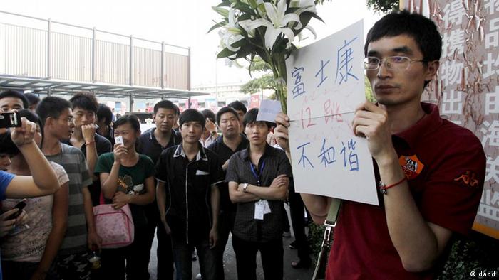 Workers surround a local resident holding flowers and a sign that reads "Foxconn, twelfth jump, not harmonious" to mourn the workers who committed suicide at the entrance of the Foxconn complex in the southern Chinese city of Shenzhen Thursday, May 27, 2010. A young man became the 10th worker to jump to his death at a Foxconn Technology Group factory in southern China, just hours after the company's chairman toured the plant that makes iPods and other top-selling gadgets, state-run media said.  (ddp images/AP Photo/Kin Cheung)