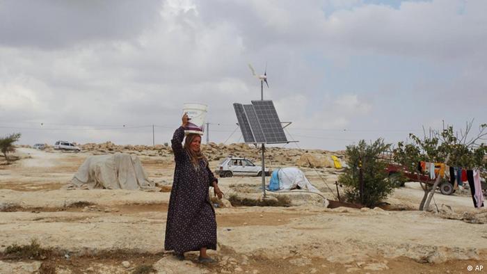 A Palestinian woman carries a bucket on her head as she passes a solar panel, in the West Bank village of Susya near Hebron