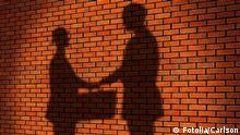 The shadows of two men shaking hands and exchanging a briefcase presumably full of cash contrast against a red brick wall
(Photo: © Carlson)