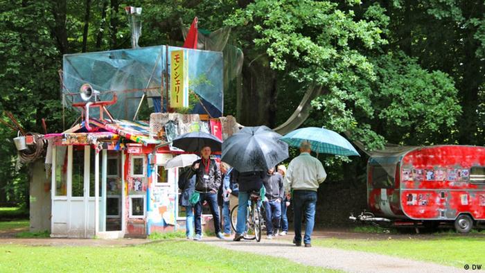 Person holding an umbrella walking past an artwork at the Karlsaue 