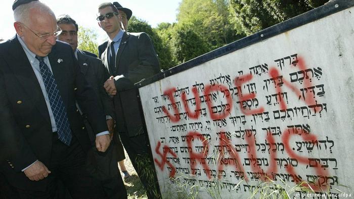 A man wearing a yarmulke gazes upon a Jewish grave defaced by graffiti 