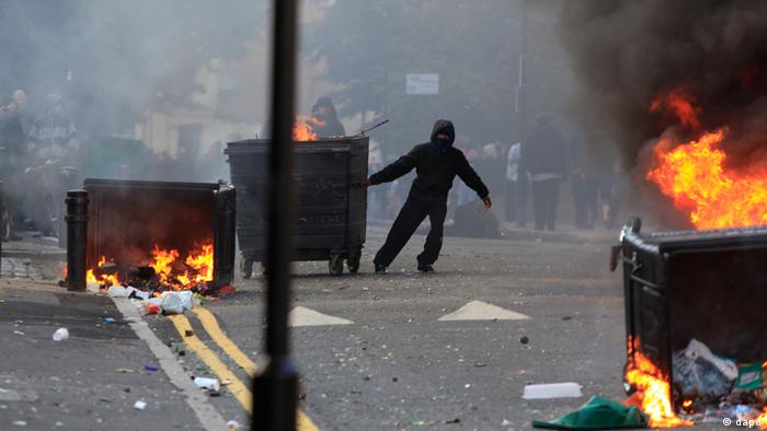 A masked youth pulls a burning garbage bin set on fire by rioters in Hackney, east London, Monday Aug. 8, 2011