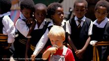 Black school children with a white boy eating an ice cream cone in front of them, Johannesburg, South Africa.