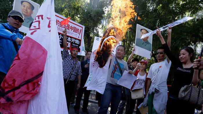 Chinese protesters burn a Japanese flag near posters claiming Diaoyu islands, as known in China and Senkaku in Japan, belong to China and to fire upon Japan during a protest near the Japanese Embassy in Beijing, China, Tuesday, Sept. 18, 2012. The 81st anniversary of a Japanese invasion brought a fresh wave of anti-Japan demonstrations in China on Tuesday, with thousands of protesters venting anger over the colonial past and a current dispute involving contested islands in the East China Sea. (Foto:Ng Han Guan/AP/dapd)