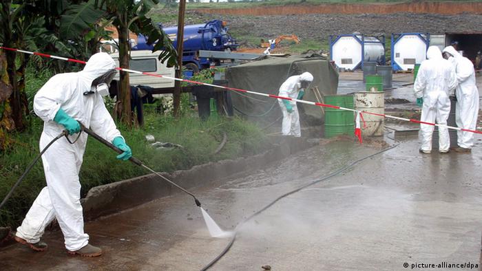 Workers in white biohazard suits spray the ground in an attemp to remove toxic chemicals.

EPA/LEGNAN KOULA