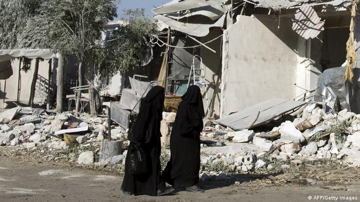 women walk past the rubble of a building in Aleppo, Syria