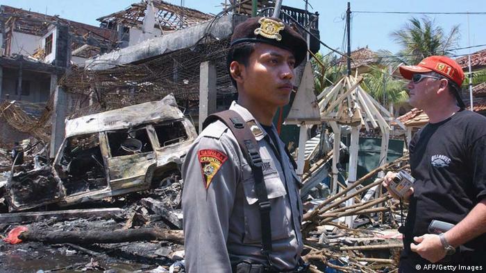  A foreign tourist (R) looks at the destroyed building of what remains of the Padi club the day after a bomb blast in Denpasar, on the Indonesian island of Bali, 13 October 2002. The huge car bomb ripped through two bars late 12 October packed with foreign tourists on the Indonesian resort island of Bali, killing at least 182 people in an attack blamed on terrorists  (Photo: AFP Getty Images) 