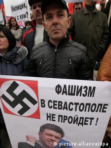 A middle-aged man wearing a black jacket and black baseball cap looks forlorn as he holds a white poster bearing a nazi swastika and a picture of a member of the nationalist Svoboda party.
(Photo: Alexei Pavlishak)