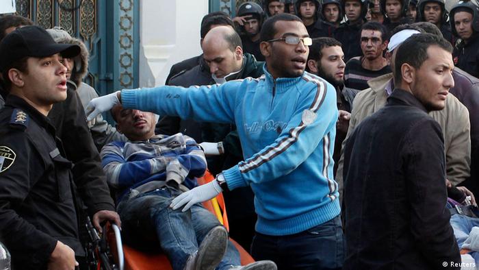 A clean-cut Egyptian man wearing a bright blue sweatshirt and modern eyeglasses points at an injured man next to him on a stretcher. 
(Photo: REUTERS/Asmaa Waguih)