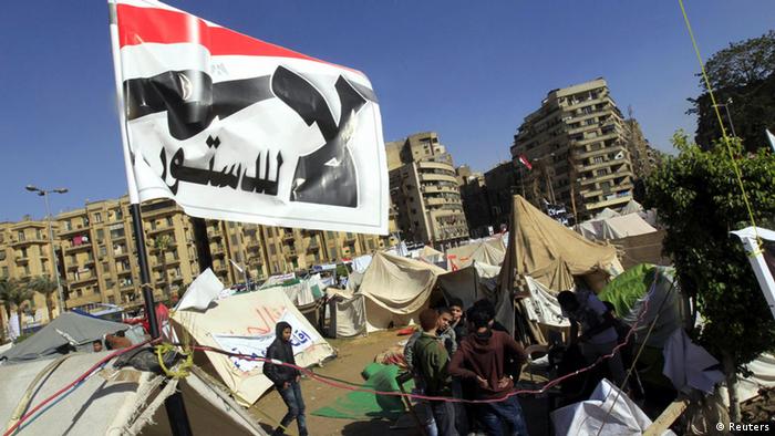 Anti-Mursi protesters sit outside their tents, below a flag that reads, No, to Constitution at Tahrir Square in Cairo December 10, 2012. The Egyptian government has given the military the authority to arrest civilians to help safeguard a constitutional referendum Islamist President Mohamed Mursi has planned for Saturday, the official gazette said. REUTERS/Mohamed Abd El Ghany (EGYPT - Tags: POLITICS CIVIL UNREST)