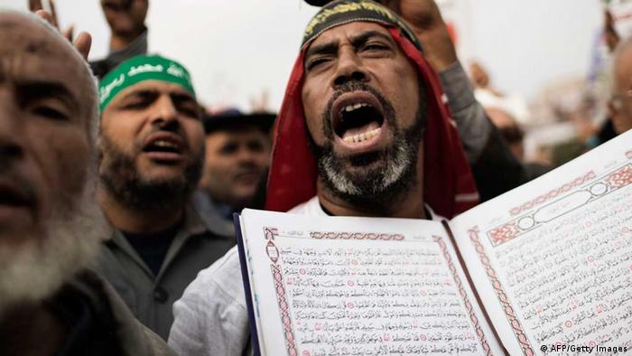A bearded, Middle Eastern man wearing a red hair dress holds an opened Koran with Arabic text toward other protestors at a large outdoor demonstration.
(Photo: MARCO LONGARI/AFP/Getty Images) 