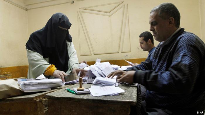 An older Egyptian woman wearing a black headscarf passes her vote to two men sitting at a table in a small room.
(Photo:Amr Nabil/AP/dapd)