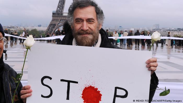 Ali Ferzat holds a placard reading “stop”