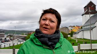 A woman in green looks off camera as she speaks, with the coastal scenery of a small seaside town in the background.
(Photo: DW / Lars Bevanger)