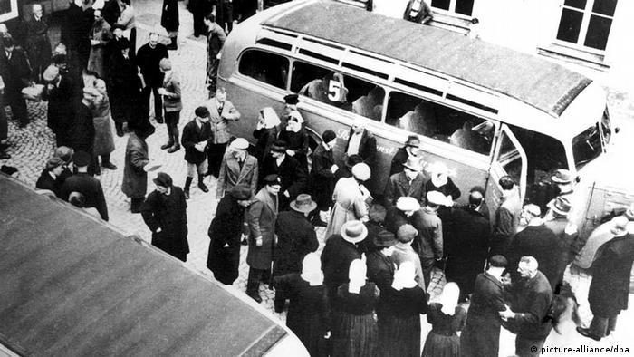 Fotografija prikazuje brojne žrtve nacističke eutanazije. Ljudi stoje ispred autobusa kod bolnice za mentalna oboljenja i čekaju na prijevoz do mjesta gdje će biti ubijeni. 