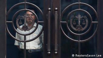 A man looks out behind the door of the Jinan Intermediate People's Court building during the trial of disgraced Chinese politician Bo Xilai in Jinan, Shandong province August 23, 2013. China's state media called Bo, the former Communist Party chief of the Chongqing region, arrogant and a liar for his robust defence at his landmark trial, the country's highest profile court case since the Gang of Four was dethroned in the 1970s and put in the dock. REUTERS/Jason Lee (CHINA - Tags: POLITICS CRIME LAW CIVIL UNREST SOCIETY)