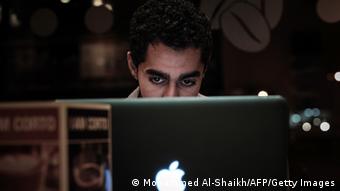 A man peers over the top of his computer screen