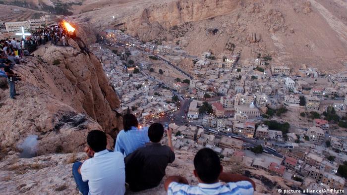 A half-dozen people sit high above a village tucked into a sandstone valley.Photo: Bassem Tellawi