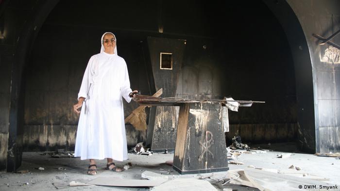 Standing next to a charred alter, the white robes of a nun of Middle Eastern descent contrast strikingly with the black, burned-out shell of a former Franciscan school. (Photo: Markus Symank / DW)