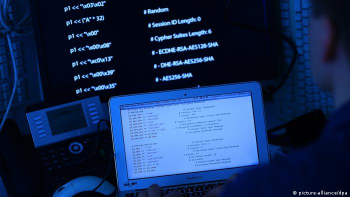 A man sits in front of a laptop screen above which a larger screen shows source code