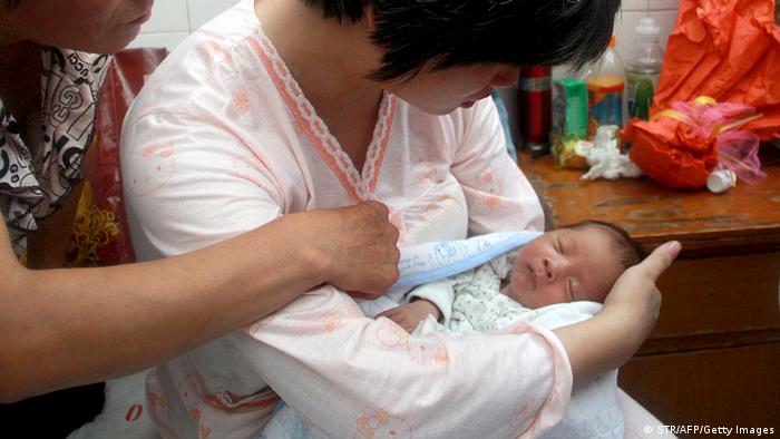 This picture taken on August 5, 2013 shows a woman surnamed Dong (C) holding her newborn baby surrounded at a hospital in Fuping County, central China's Shanxi province. A baby boy allegedly sold by the doctor who delivered him in China has been reunited with his parents, state media reported on August 6, in a case highlighting the problem of child trafficking. CHINA OUT AFP PHOTO (Photo credit should read STR/AFP/Getty Images)