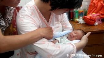 This picture taken on August 5, 2013 shows a woman surnamed Dong (C) holding her newborn baby surrounded at a hospital in Fuping County, central China's Shanxi province. A baby boy allegedly sold by the doctor who delivered him in China has been reunited with his parents, state media reported on August 6, in a case highlighting the problem of child trafficking. CHINA OUT AFP PHOTO (Photo credit should read STR/AFP/Getty Images)