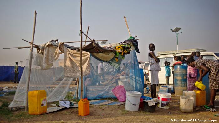 South Sudanese refugees standing outside a tent made of a mosquito net