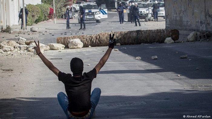 A man sits on the road in front of police, his hands in the air, making the sign of peace