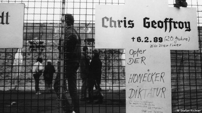 A cross of remembrance has the name Chris Gueffroy had written on it in a black-and-white photograph.