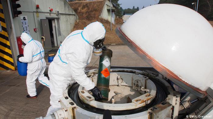 Men in biohazard suits place chemicals into a large container
