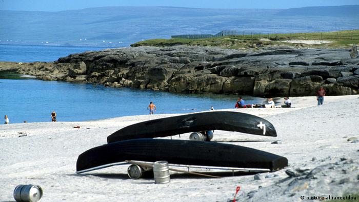 Zwei Boote liegen umgedreht am Strand der irischen Aran Inseln. Der Sand ist fast weiß und das Meer ist hellblau. (Foto: Picture-alliance/dpa)
