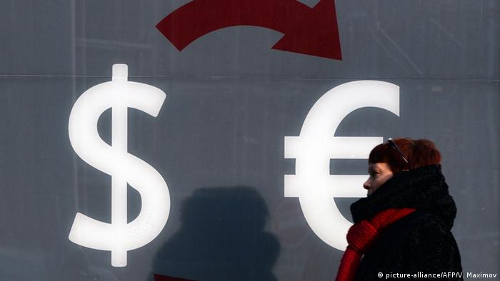 Женщина на фоне стены, на которой нарисованы символы доллара и евро