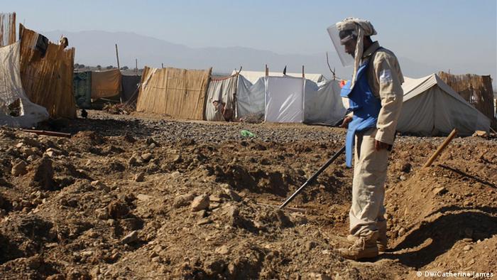 A deminer checks uncleared land in the Golan refugee camp in Khost province, Afghanistan just meters from where refugees have set up makeshift homes