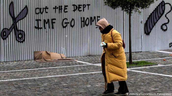 A woman walks past graffiti that reads 'Cut the debt IMF go home' on a fence around the Academy of Sciences in Athens