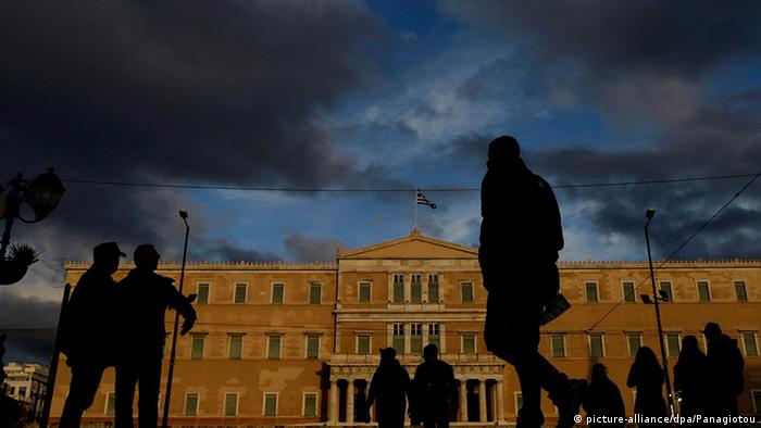 People walk in front of the Greek Parliament building in Athens under a dark, ominous sky