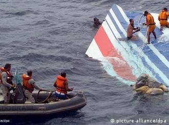 Sailors in an inflatable dinghie and perched on floating wreckage